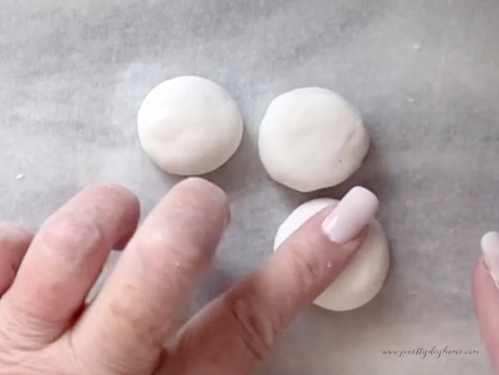 Rolled air dry clay beads being flattened by hand.