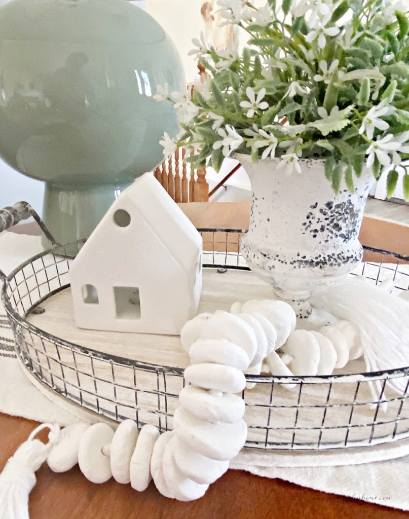 DIY air dry clay beads sitting in an arrangment with a green lamp, a vase with greenery, and a white porcelain house decoration.