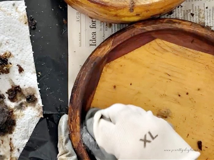 Stripping a wooden bowl with wood stripper and steel wools.  You can see the wooden bowl with a gloved hand holding the steel wool and scrubbing.