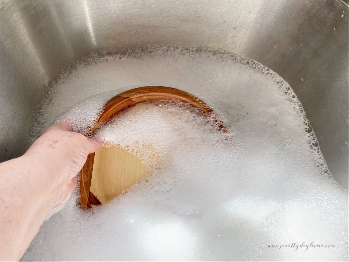 Washing a vintage wooden bowl in a sink full of warm sudsy water.