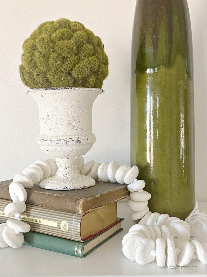 A string of homemade DIY clay beads.  The clay beads are decorating an arrangment with old books, vintage vase and greenery.