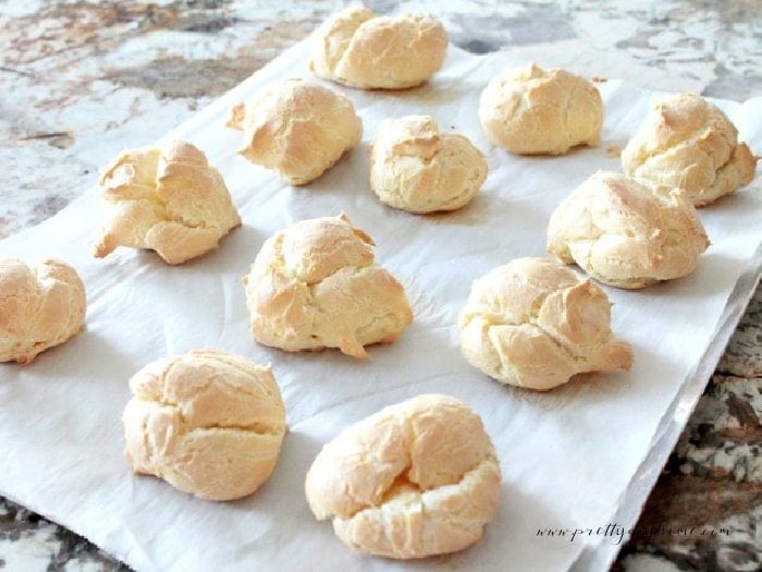 Cream puffs cooling to room temperature on a parchment lined baking sheet.