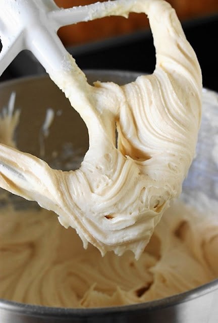 A caramel cream cheese frosting that is thick and smooth hanging from a large mixer beater.