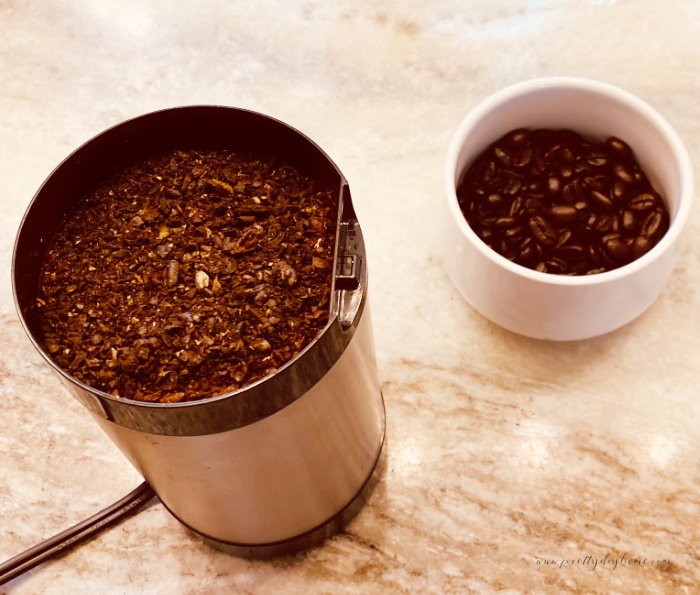 A half cup of whole coffee beans, and a grinder filled with freshly ground coarse coffee.