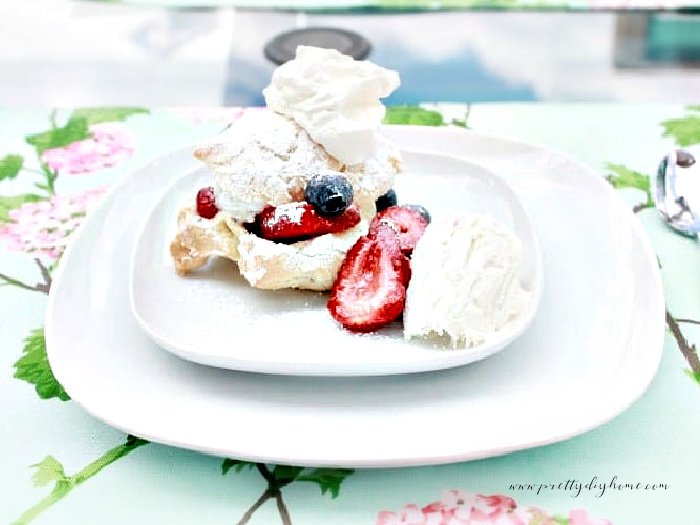 Homemade cream puffs being served on a white plate with fresh whipping cream and berries.