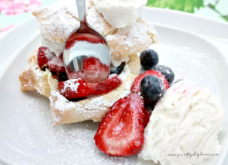 A cream and berry filled cream puff recipe being served on a white plate with ice cream for summer.