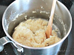 Cooking choux pastry over a stove top, stirring with a wooden spoon.