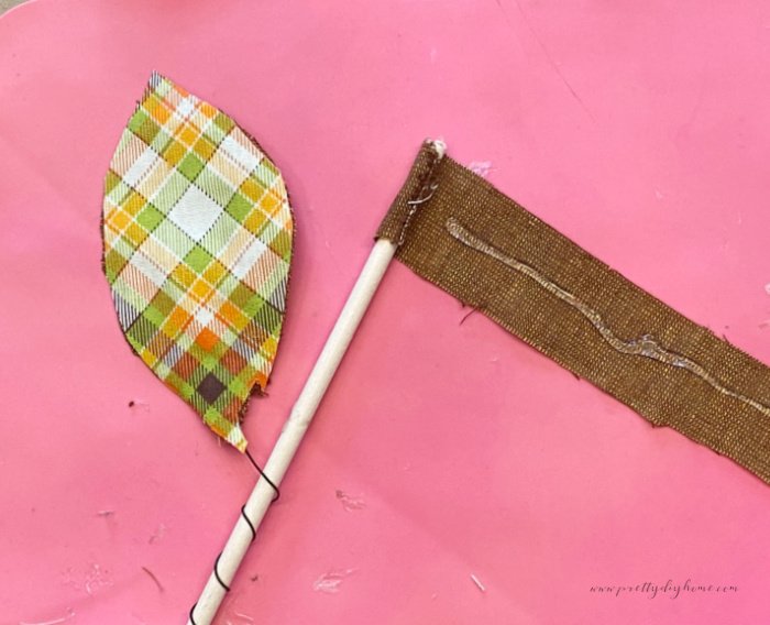 A handmade fabric leaf with its wire wrapped around a dowel.  