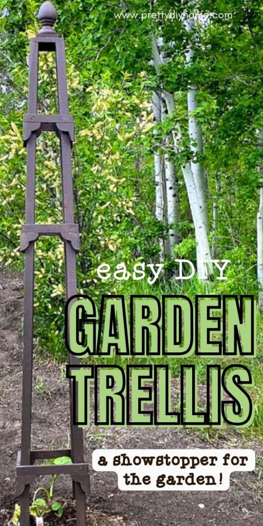 A large 7 foot DIY garden obelisk sitting in a garden with lots of tree in the background.