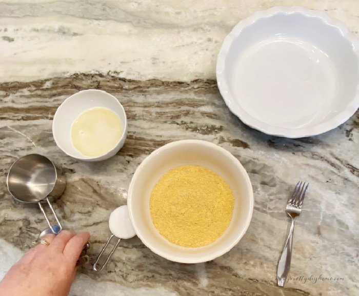 An overhead picture of the ingredients for making graha cracker crust. You can see a large pie plate, melted butter, sugar and graham crackers set out neatly on a counter.