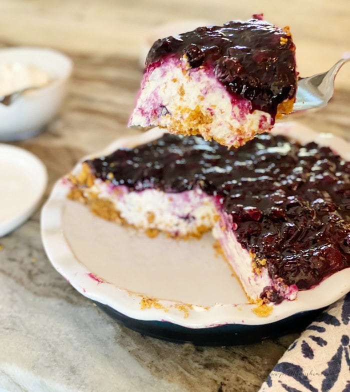 A cream cheese pie recipe that been cut and one piece is being lifted out of the center of the pie.