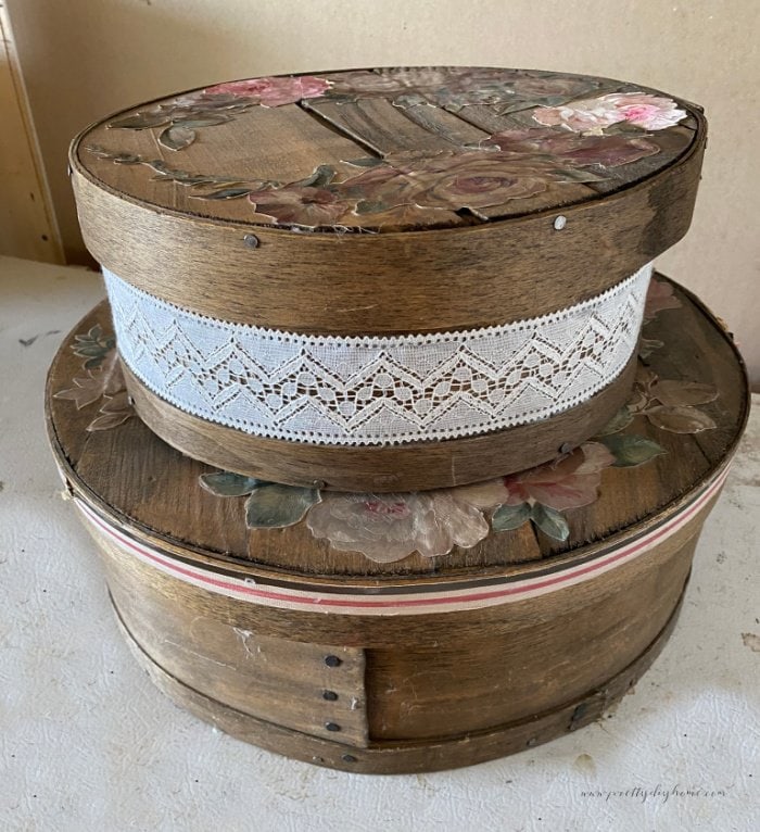 Two antique cheeseboxes in dark brown stain. Both cheeseboxes have lace, ribbon and floral stickers on them.