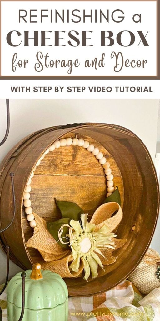 A refinished wood cheese box in walnut stain with a sunflower wreath decorating it.