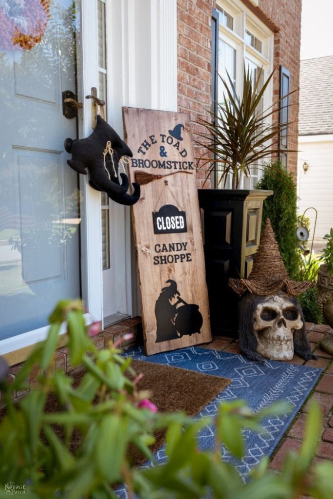 Outdoor Halloween candy shoppe wood sign on a front porch, with a large skeleton wearing a witches hat beside it.