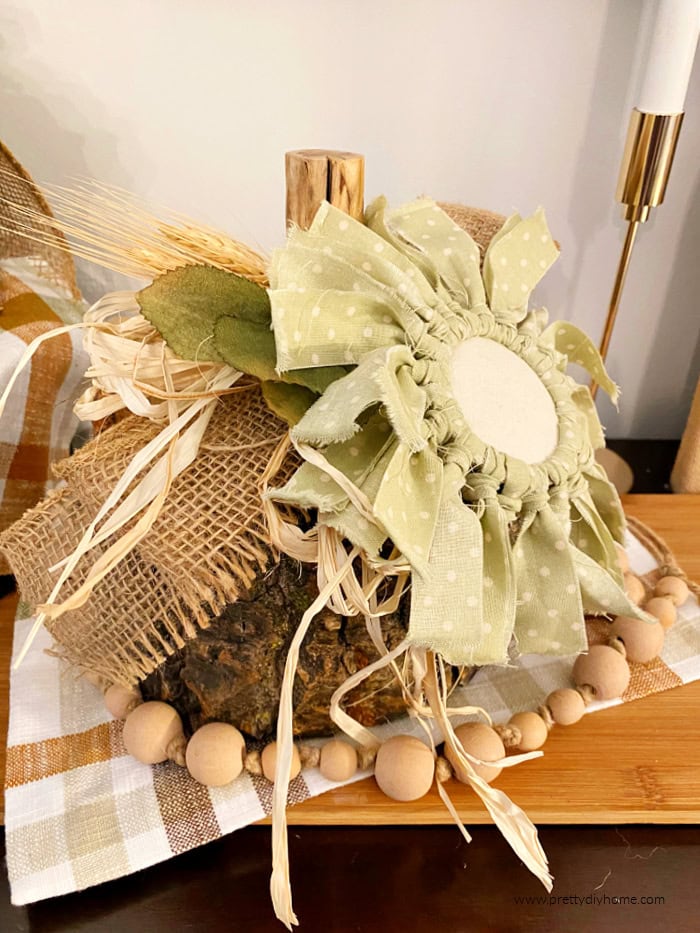 A log pumpkin in natural colors with a branch stem, and decorated with a fabric flower made using a mason jar ring, and soft green polka dot fabric.