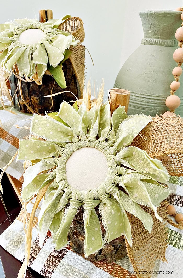 Two DIY wood pumpkins made out of logs with mason jar fabric flowers for decoration. The natural brk is intact.