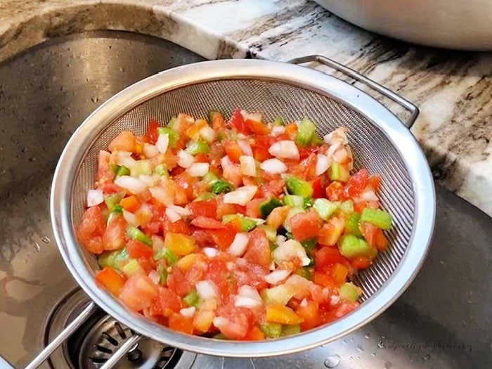 Draining salsa ingredients in a fine sieve over the kitchen sink.  Part of a canning tomato salsa recipe.