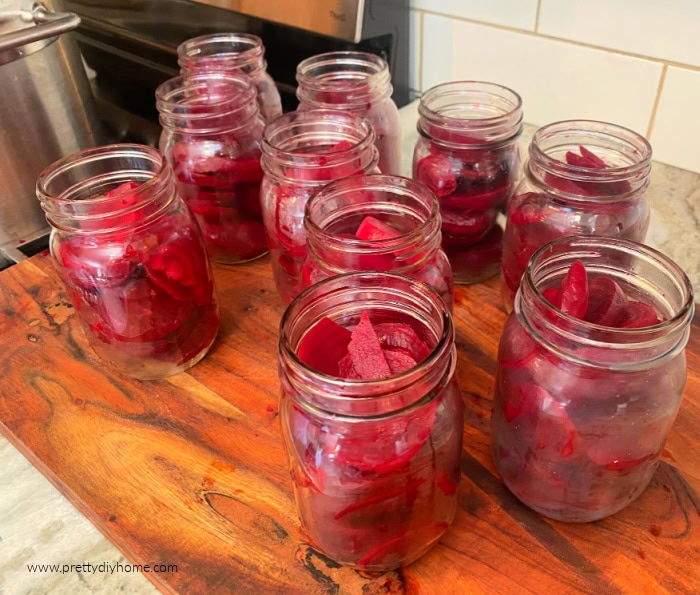 Eight mason jars sitting on a wooden cutting board.  Each jar is filled with cooked and sliced beets, but the spiced pickling brine has not been added yet.