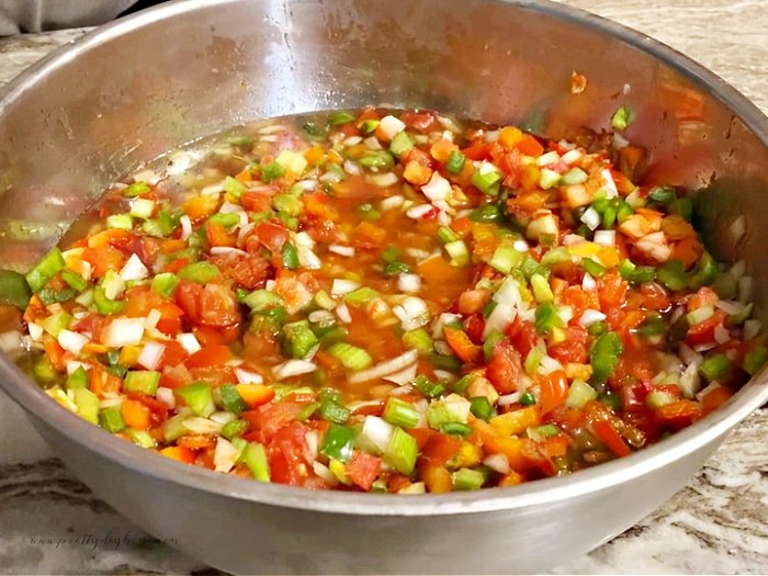 A large stainless steel bowl filled with coarsely chopped tomatoes and other vegetables for making homemade canned salsa.