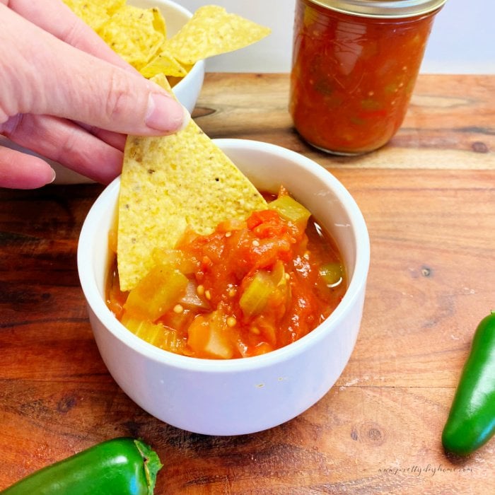 A small bowl of freshly made canned tomato salsa showing the large chunks of vegetables. The person is dipping a tortilla chip into the salsa.