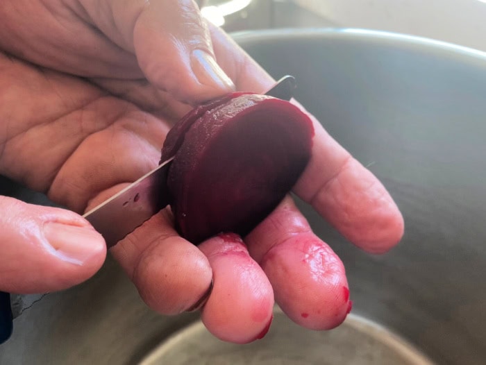 Freshly peeled boiled beets with the skin removed being sliced by hand over a sink of cold water.