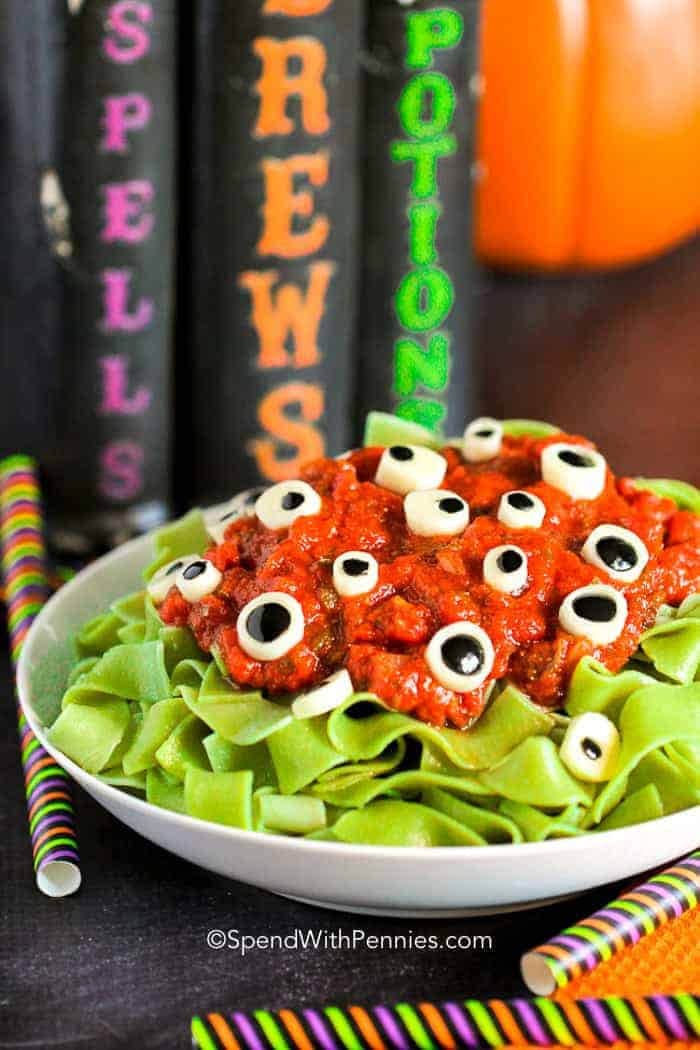 A Halloween noodle recipe with large green egg noogles covered with red meat sauce and decorated with cheese rounds and olive bits that look like eyeballs.