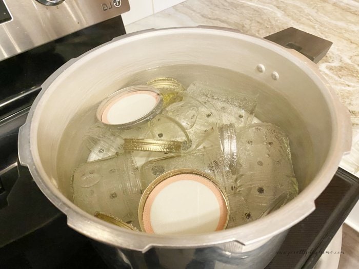 A large pot filled with boiling water, canning jars, lids and rings beign sterilized for a tomato salsa recipe.