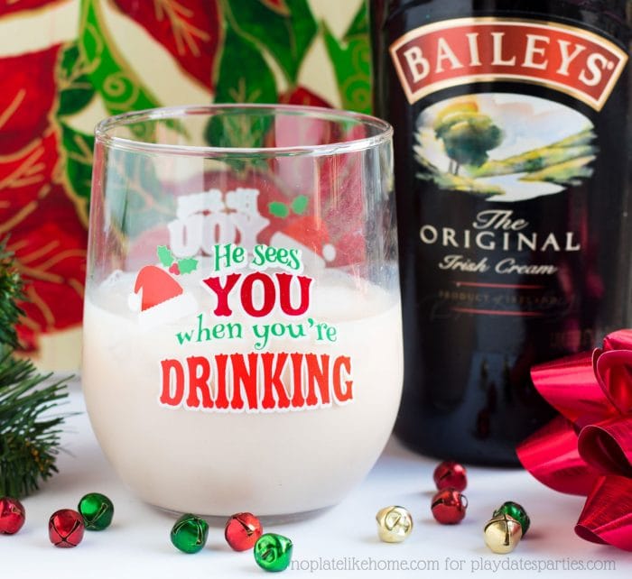 A glass filled with a Baileys Buttersock almond cocktail being served in a fun Christmas glass and a bottle of Bailey's sitting beside.