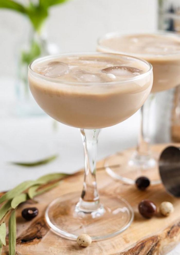 Two stemmed martini glassesesp filled with ice and esspresso and Baileys cocktail.  The two glasses are sitting on a cutting board.