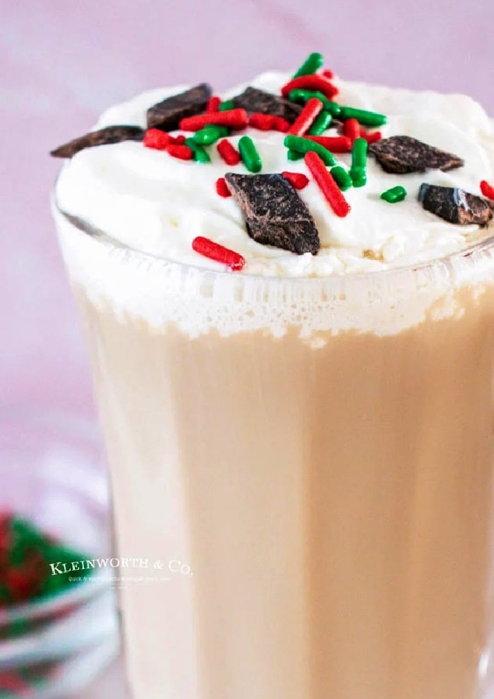 A clear cup filled with a boozy Christmas coffee you can see a bit of foamy milk on top and Christmas sprinkles