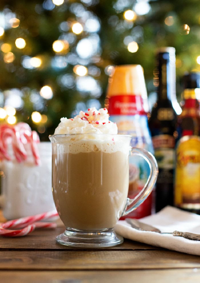 A delicious Christmas cofee recipe  being served in a clear mug with a large swirl of whipped cream and red sprinkles on top.  The background has a bottle of Bailey's and Kahlua.