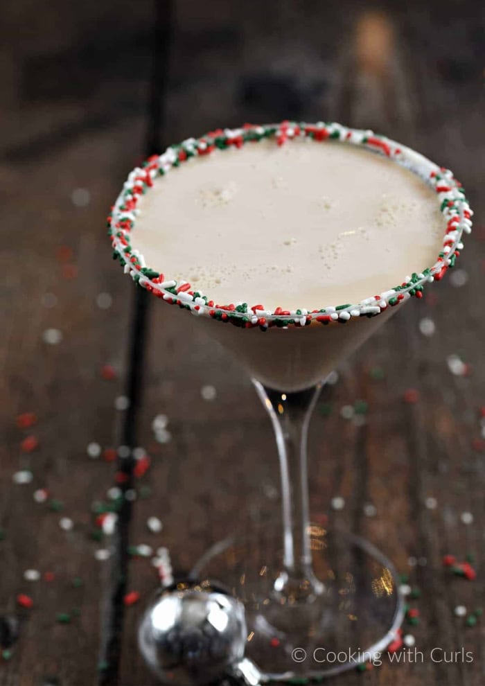 A creamy Christmas cookie martini served in a martini glass and rimmed with Christmas sprinkles.  The background is dark wood.