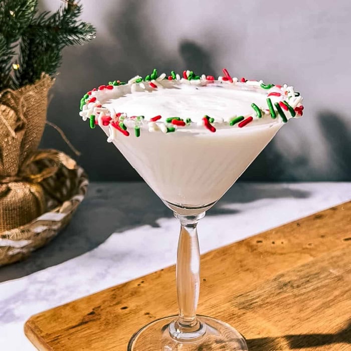 A martini glass rimmed with green red and white Christmas sprinkles.  The glass is full holding a Christmas sugar cookie martini cocktail recipe.