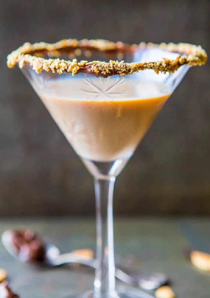 A creamy chocolate martini with Baileys and nutella.  The martini glass is rimmed in nutella and crushed graham cracker. then filled with the Christmas cocktail recipe.  The background is dark grey.