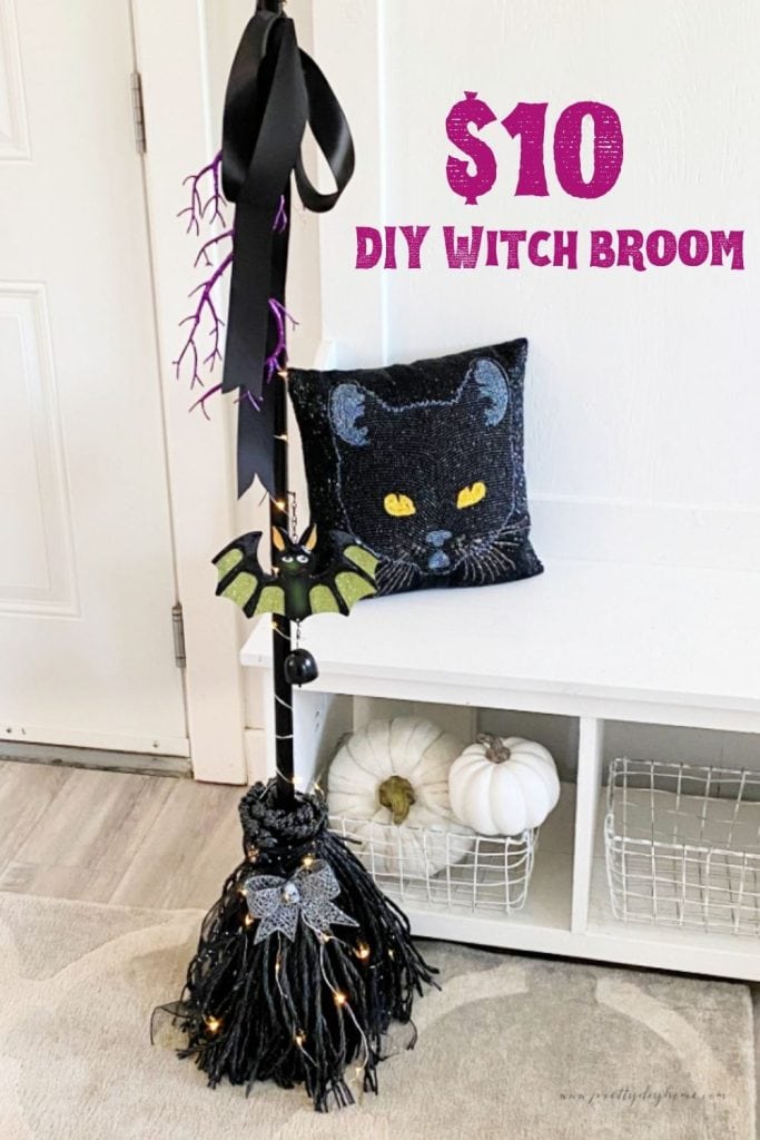 A sparkling black DIY witch broom thats standing on its own with lights, sparkly ribbons, and a glitter covered bat.