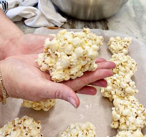 A large popcorn ball laying on my hand after being shaped. You can see the rest of the large popcorn balls behind sitting on parchment paper.