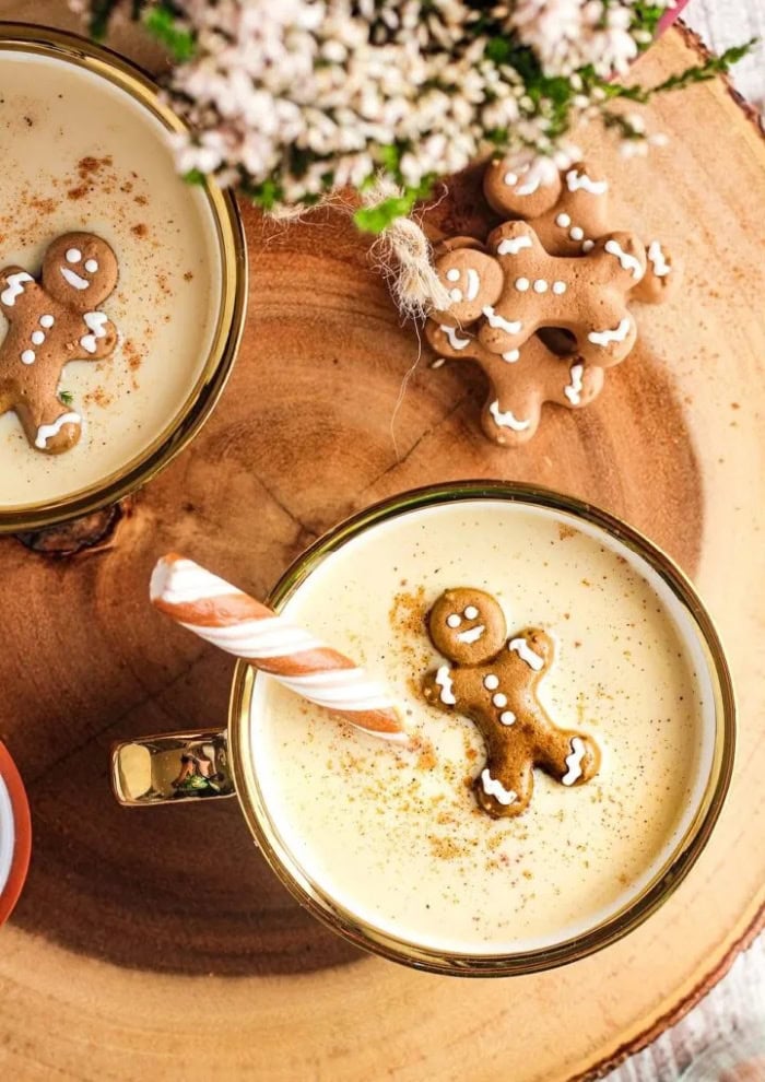 The top view of two glasses of eggnog with Bailey's irish cream.  Each Christmas drink is covered with a miniature gingerbread floating on top and a candy cane to stir.