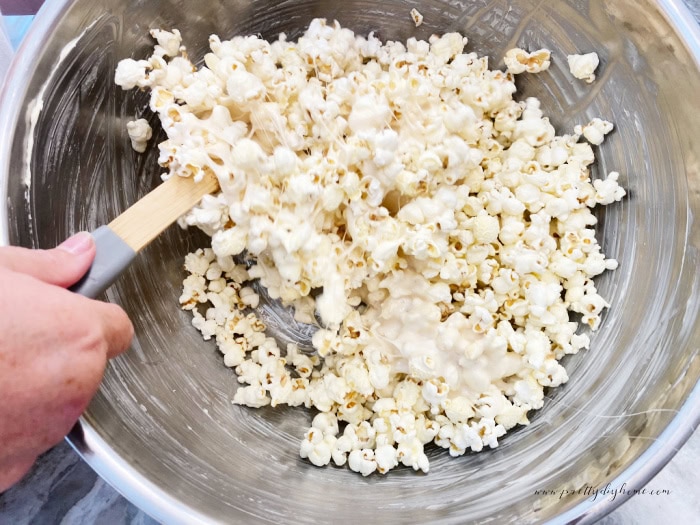 A large steel bowl thats been greased with butter and then filled with fresh popped popcorn and melted marshmallow mixture. The popcorn is being stirred for making popcorn balls.