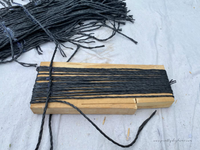 Making bundles of faux witch broom bristles using black plastic dollar tree rope.  The rope is being wrapped around a piece of wood, and their is a cross piece of rope across the top for tying it to the broom handle.