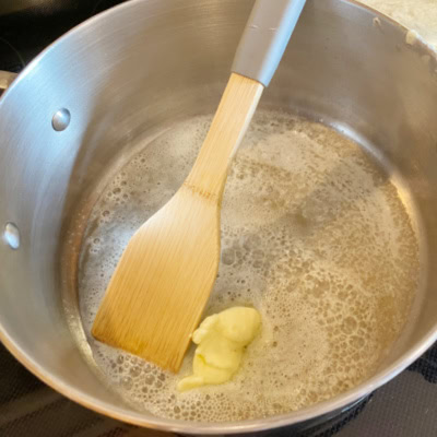 A saucepan with melted butter and a wood spatula, while making a popcorn ball recipe.