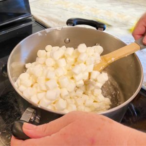 Stirring miniature marshmallows while they melt to prevent them from burning while making Halloween popcorn balls.