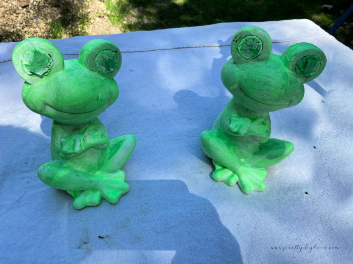 Two garden frogs painted in a very bright neon green paint for DIY Halloween decoration.