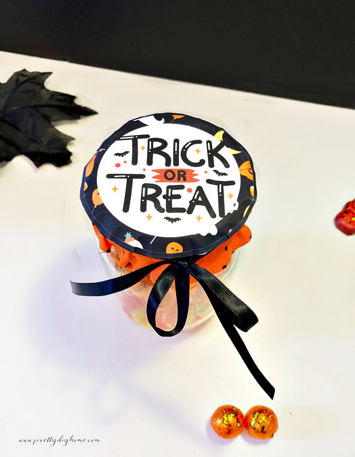 A trick or treat Halloween label free printable. The tag round and covering the top of a mason jar filled with Halloween candy.