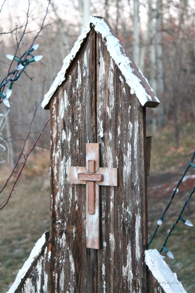 A closeup of a rustic wood church Christmas decoration. The church as a metallic cross and the front, the wood has lots of texture and is decorated with faux snow.