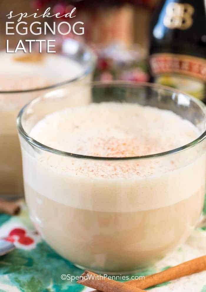 Two clear round glass mugs will with spiked eggnog latte.  You  can see the layers of coffee and foamy cream.