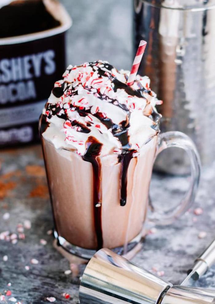 A peppermint mudslide Baileys Christmas cocktail covered with a large layer of whipped cream, red sprinkles and chocolate syrup.  Its served in a large glass with a red striped straw.