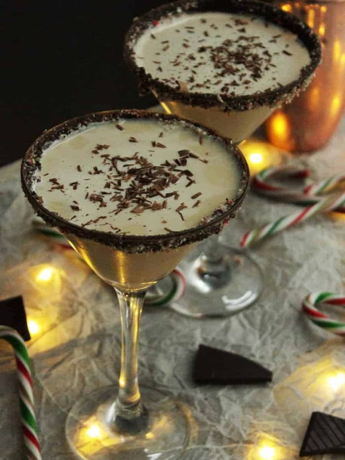 Two Bailey's candy cane cocktails in a dark setting with sparkling warm light Christmas lights.