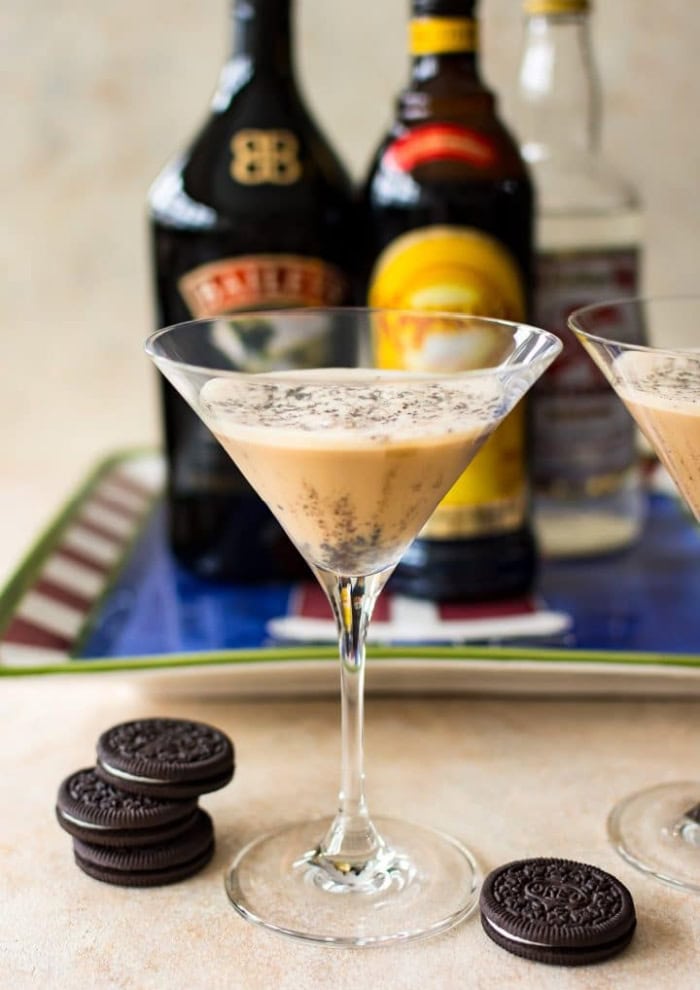 A Christmas cookie cocktail recipe served in an martini glass.  The glass is surrounded with Oreo cookies and a bottle of Bailey's and Kahlua.