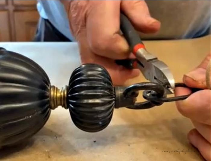 The top of a garage sale chandelier being dismantled using wire cutters. The chain and the wire on the top of the chandelier are being cut off.