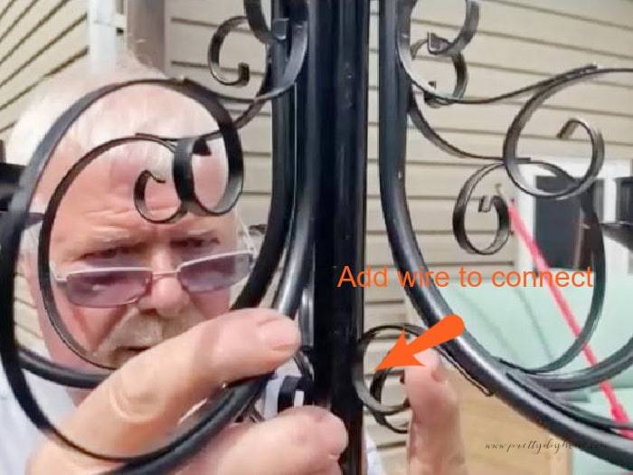 A man connecting a black Halloween chandelier to the top of a pole while making a scary DIY Halloween decoration for outdoors.